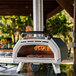 An Ooni Karu 16 pizza oven on a table with a pizza cooking inside.