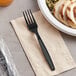 A black plastic Visions heavy weight fork on a napkin next to a bowl of food.