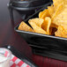 A black square plastic basket filled with chips and dip on a table in a restaurant.