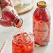 A hand pouring Harney & Sons Organic Cranberry Juice from a glass bottle into a glass with ice.