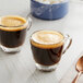 A glass cup of Lavazza Espresso Maestro Ristretto coffee next to a copper spoon and bowl of sugar.