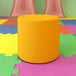 A yellow cylindrical Flash Furniture Nicholas ottoman on a colorful surface.