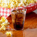 A Fineline tall clear hard plastic tumbler filled with soda and ice next to a basket of popcorn.