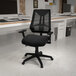 A Flash Furniture Ivan black mesh high-back office chair with adjustable arms in a room with a computer.