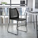 A Flash Furniture black stacking chair with a black sled base in front of a white table.