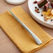 An Acopa Lore stainless steel steak knife on a napkin next to a plate of food.