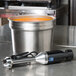A Waring Quik Stik immersion blender on a counter next to a large pot of orange liquid.