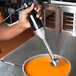 A hand holding a black and silver Waring Quik Stik hand blender over a bowl of orange liquid.