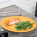 A GET Tropical Yellow oval melamine platter with a piece of salmon and green vegetables on it.