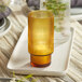 An Acopa Lore amber ribbed glass tealight/votive holder on a tray with a lit yellow candle.