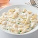 A white plate of pasta with peas and Foothill Farms Alfredo sauce.