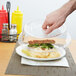 A hand holding a Carlisle clear polycarbonate plate cover over a sandwich on a white plate.