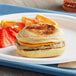 A Grand Prairie sausage and cheese muffin breakfast sandwich on a plate with orange slices.