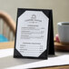 A black A-frame table tent displaying a coffee house menu with lunch bites and coffee drinks, standing on a table next to a cup.