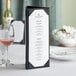 An Acopa Prime black triangular table tent with a wine list on a table.