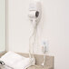 A Conair white wall mount hair dryer in a white bathroom.