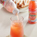 A hand pouring Tropicana Ruby Red Grapefruit Juice into a glass.