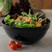 A Carlisle black acrylic bowl filled with salad, tomatoes, and lettuce on a table.