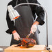 A man wearing a black and white striped apron and gloves uses a Carlisle FlexiGlow single arm bulb warmer to cut meat.