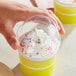 A hand holding a clear plastic container of ice cream with sprinkles.