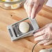 A person using a Choice rectangular aluminum hinged two-way egg slicer to cut a white egg over a bowl.