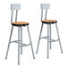 A pair of National Public Seating lab stools with Bannister Oak seats and gray steel legs.