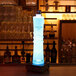 A blue bottle with a Mini Battery-Powered Solo LED Light on a cocktail bar shelf.