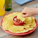 A person holding a Tostitos Thick & Hearty yellow corn chip over a bowl of salsa.