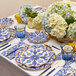 A table set with Moroccan Nights paper napkins, blue and white plates, and glasses with a fork on a napkin.