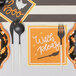 Sophistiplate Bella Black / White plastic cutlery in a bag on a table with black and orange plates.
