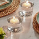 Two Hollowick white wax floating candles in glass cups on a table with green napkins.