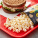 A Smartfood White Cheddar Popcorn bag on a red tray with a sandwich.