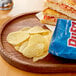 A wooden plate with a sandwich and Ruffles Original potato chips.