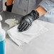 A person wearing black gloves cleaning a counter with a WypAll X50 white wiper.