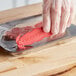 A person using a red Klever Kutter to open a plastic container of red meat.