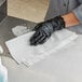 A person wearing a black glove cleaning a counter with a white WypAll wiper.