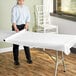 A woman rolling a white tablecloth from a Choice White Plastic Table Cover Roll