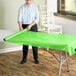 A person rolling a lime green plastic table cover onto a table.