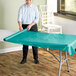 A woman rolling a teal plastic table cover onto a table.
