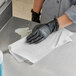 A person wearing black gloves using a WypAll X60 white wiper to clean a surface on a counter.