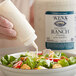 A hand pouring Ken's Fat-Free Ranch Dressing into a bowl of salad.