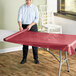 A woman rolling out a red plastic table cover onto a table.