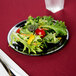 A Fineline black plastic plate with a silver banded edge holding a salad on a table with a red tablecloth.