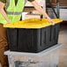 A woman in a yellow vest pushing a black and yellow Tough Box storage tote.
