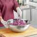 A woman in a chef's uniform mixing shredded red cabbage in a stainless steel mixing bowl.