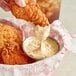 A hand holding a piece of fried chicken over a bowl of Ken's Foods Brewpub Mustard Sauce.