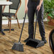 A woman using a Carlisle Duo-Pan broom and upright dustpan to sweep the floor.