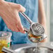 A hand using the Choice stainless steel lemon squeezer to juice an orange into a metal container.