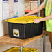 A person in a yellow vest opening a black and yellow Tough Box storage tote.