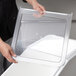 A person holding a clear plastic lid for a Cambro IBS27 ingredient bin.